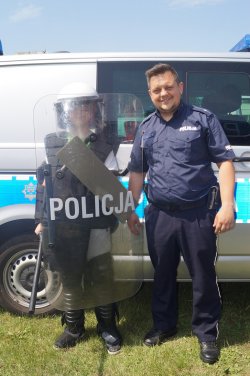 chłopiec ubrany w strój policyjny z tarczą i kaskiem pozuje z policjantem