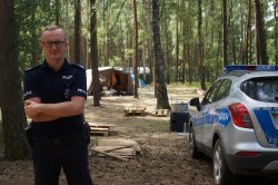 policjant przy radiowozie na tle obozu harcerskiego w lesie