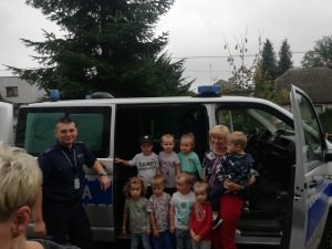 zdjęcie policjanta z grupą dzieci i wychowawców na tle radiowozu